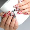 Hand holding a cup, showcasing Naillover’s red press-on nails with cherry lips and delicate bow accents