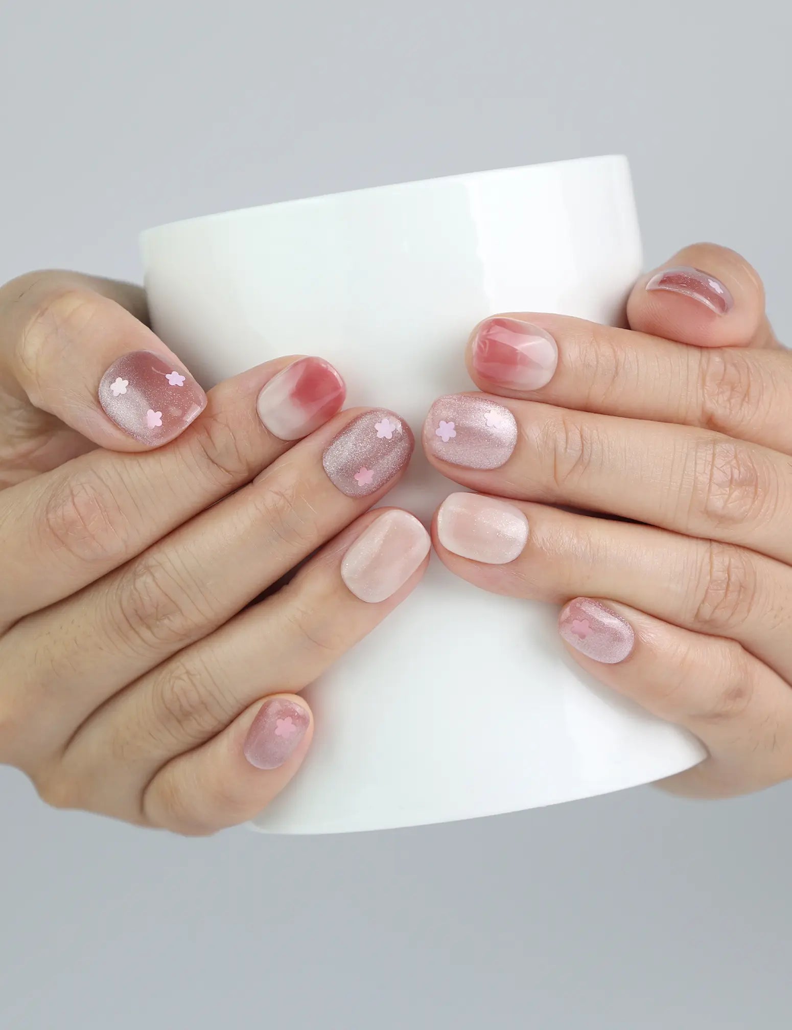 Hand holding a ceramic cup while wearing Naillover’s handmade short squoval nails with dainty pink floral designs
