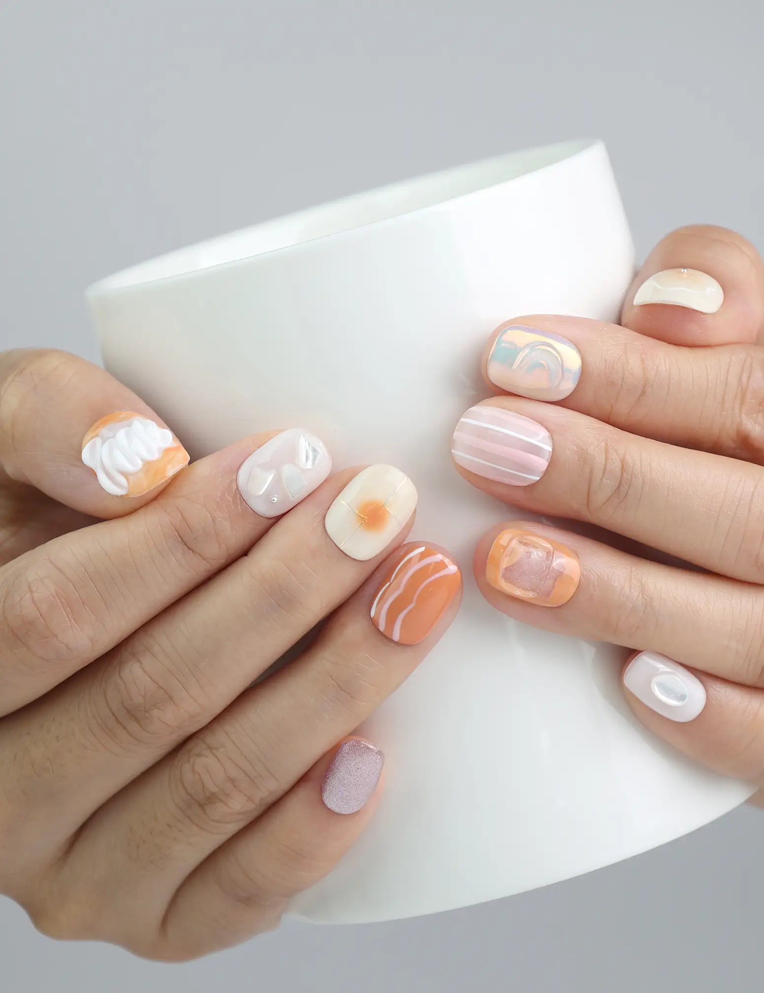 Hand holding a cup, highlighting the coral-inspired Singapore handmade nails in a tropical peach and seafoam palette by Naillover