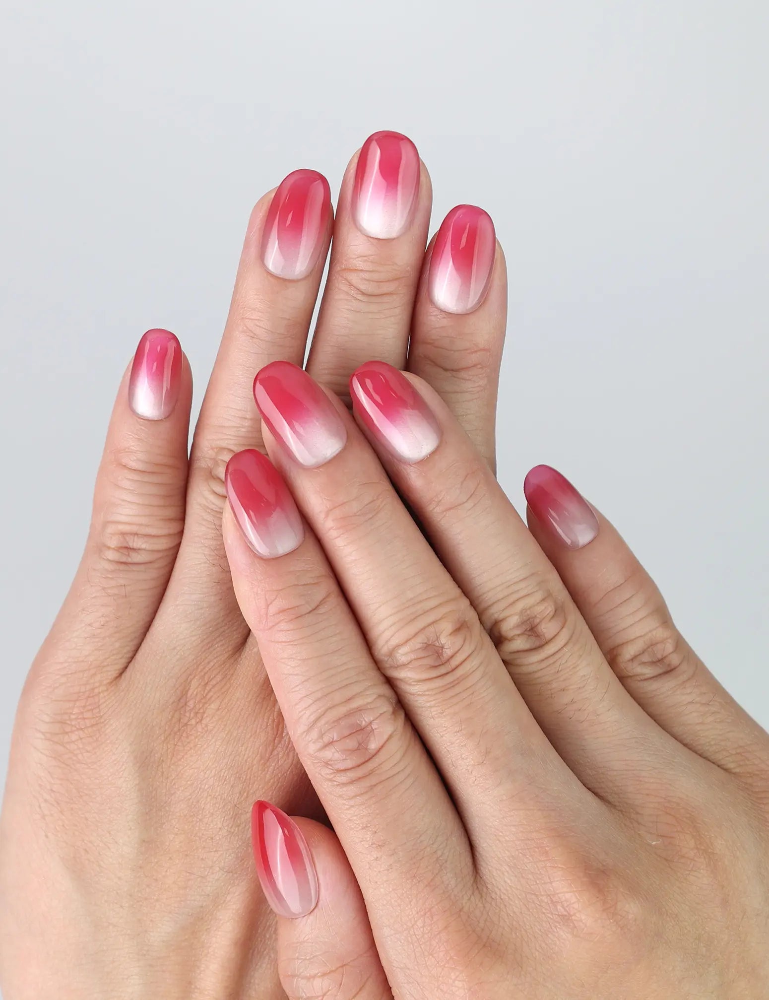 Hand model wearing short oval pink press-on nails with cat-eye shimmer and a soft pink-to-white ombré gradient