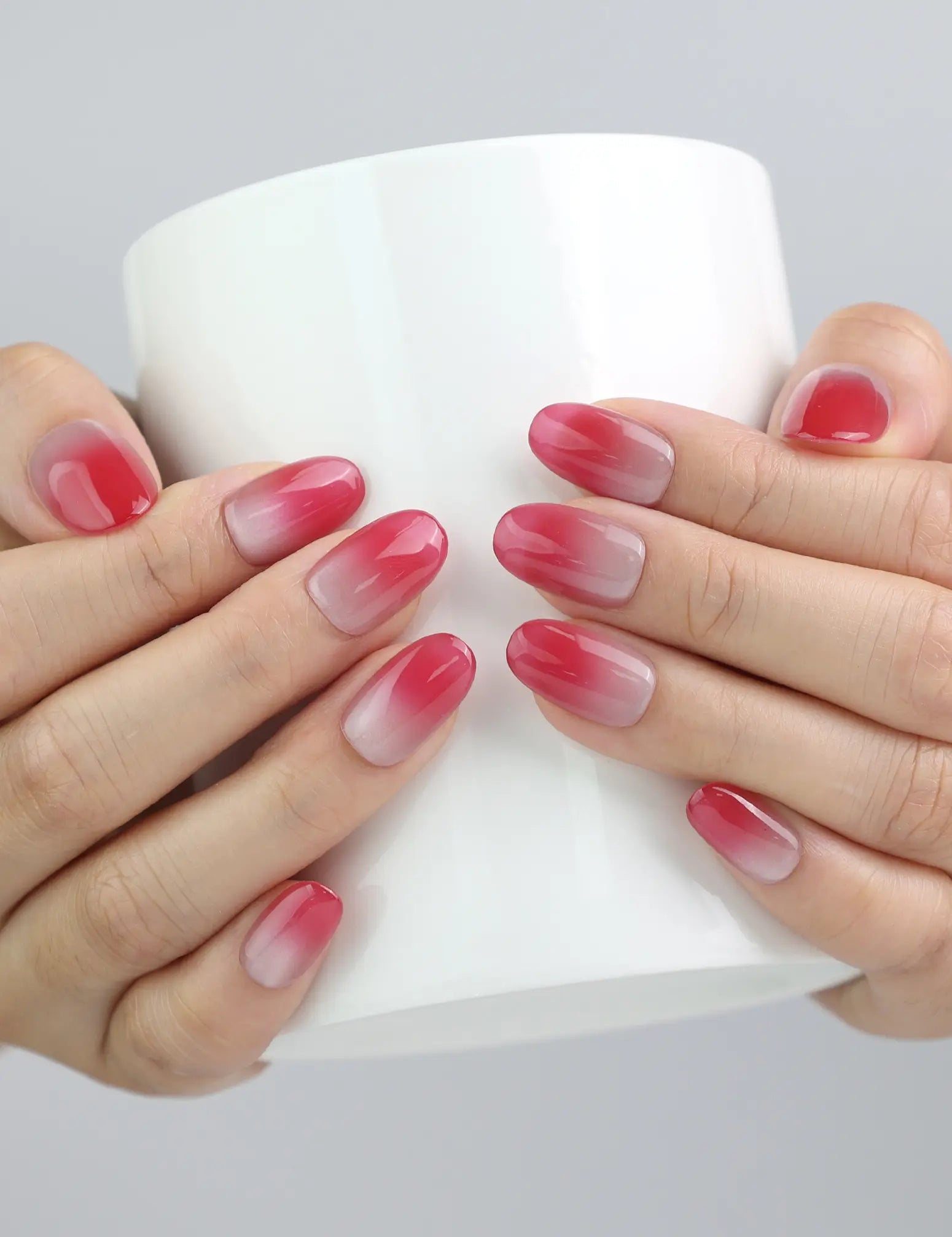 Hand holding a cup, showcasing Naillover’s gradient pink oval press-on nails with luminous cat-eye shimmer
