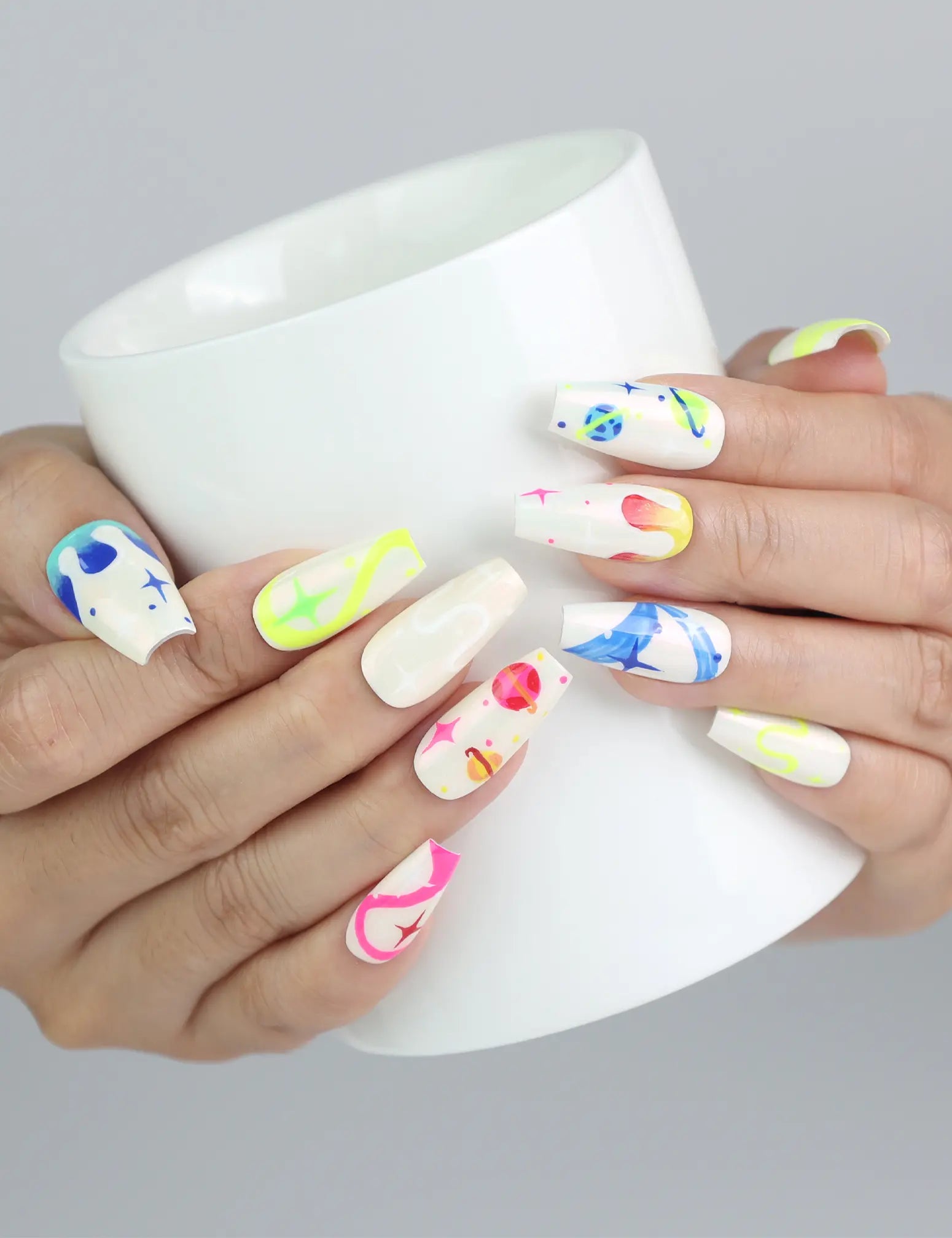 Holding a cup while wearing Naillover’s handmade coffin cute nails with multicolor abstract patterns and starry accents