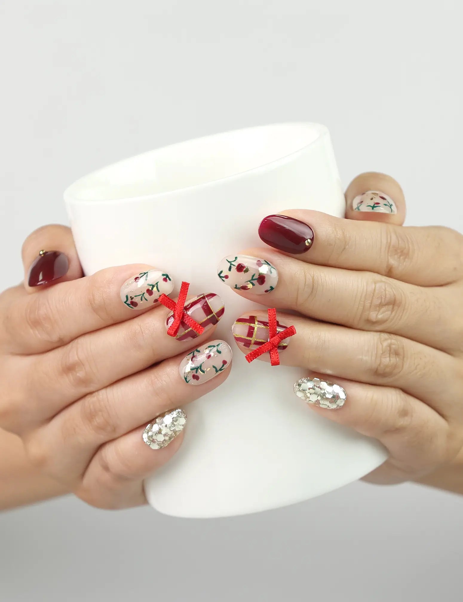 Hand holding a coffee cup while wearing Crimson Bow Singapore press on nails with white bows and festive confetti design