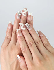 Hand model wearing medium beige coffin press-on nails with edgy zigzag patterns and crystal studs