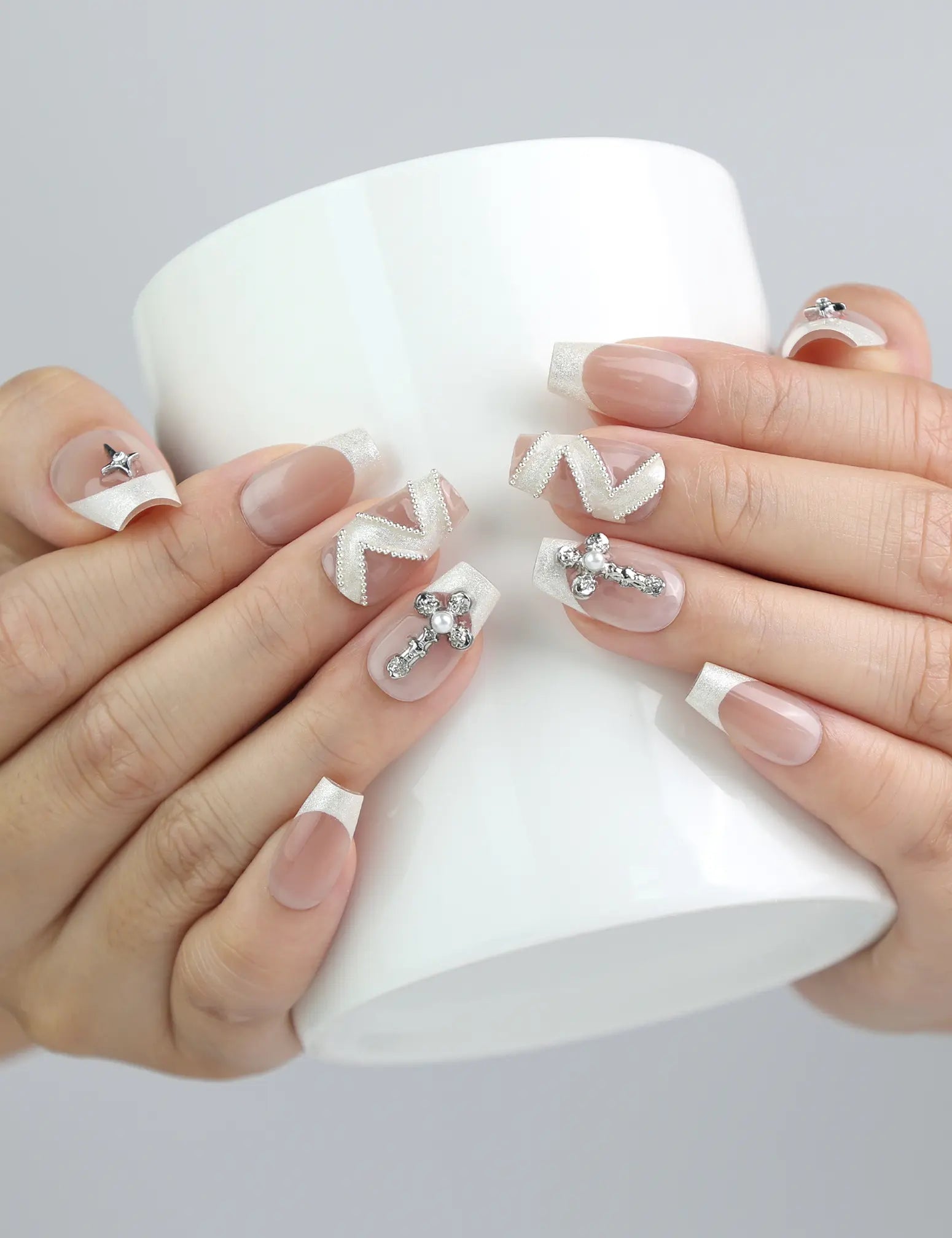 Hand holding a cup, showcasing Naillover’s beige press-on nails in coffin shape with crystal and zigzag embellishments