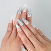 Hand model wearing blue almond-shaped press-on nails with iridescent pearl shimmer and sparkling 3D crystals