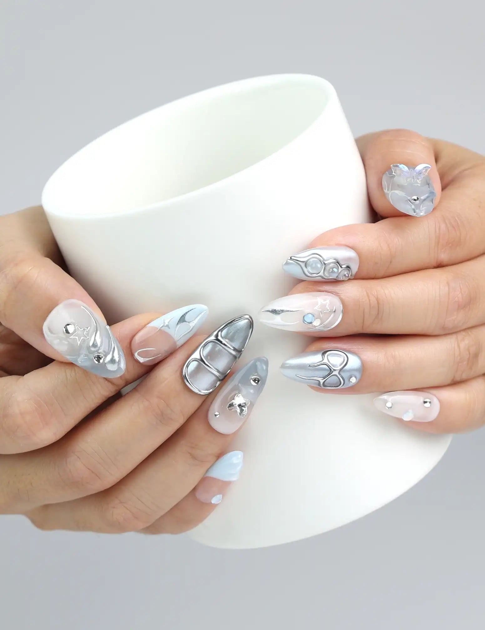 Hand holding a cup, showcasing Naillover’s pearly blue almond nails with crystal details for a frosty glam look
