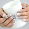 Hand holding a cup, showcasing Naillover’s pearly blue almond nails with crystal details for a frosty glam look