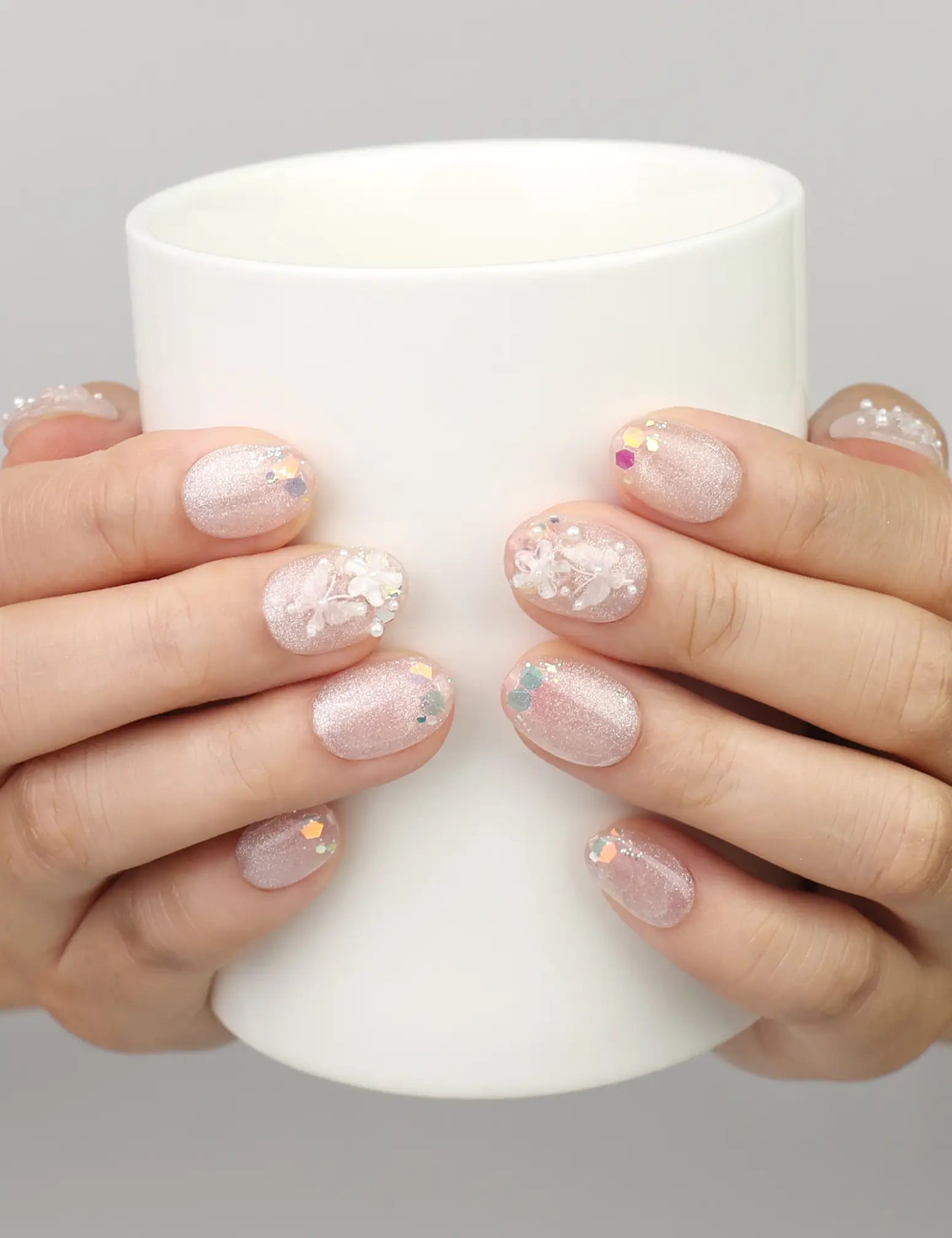 Hand holding a cup while wearing Naillover Crystal Sparkle handmade press on nails with iridescent cat eye design and colorful specks.