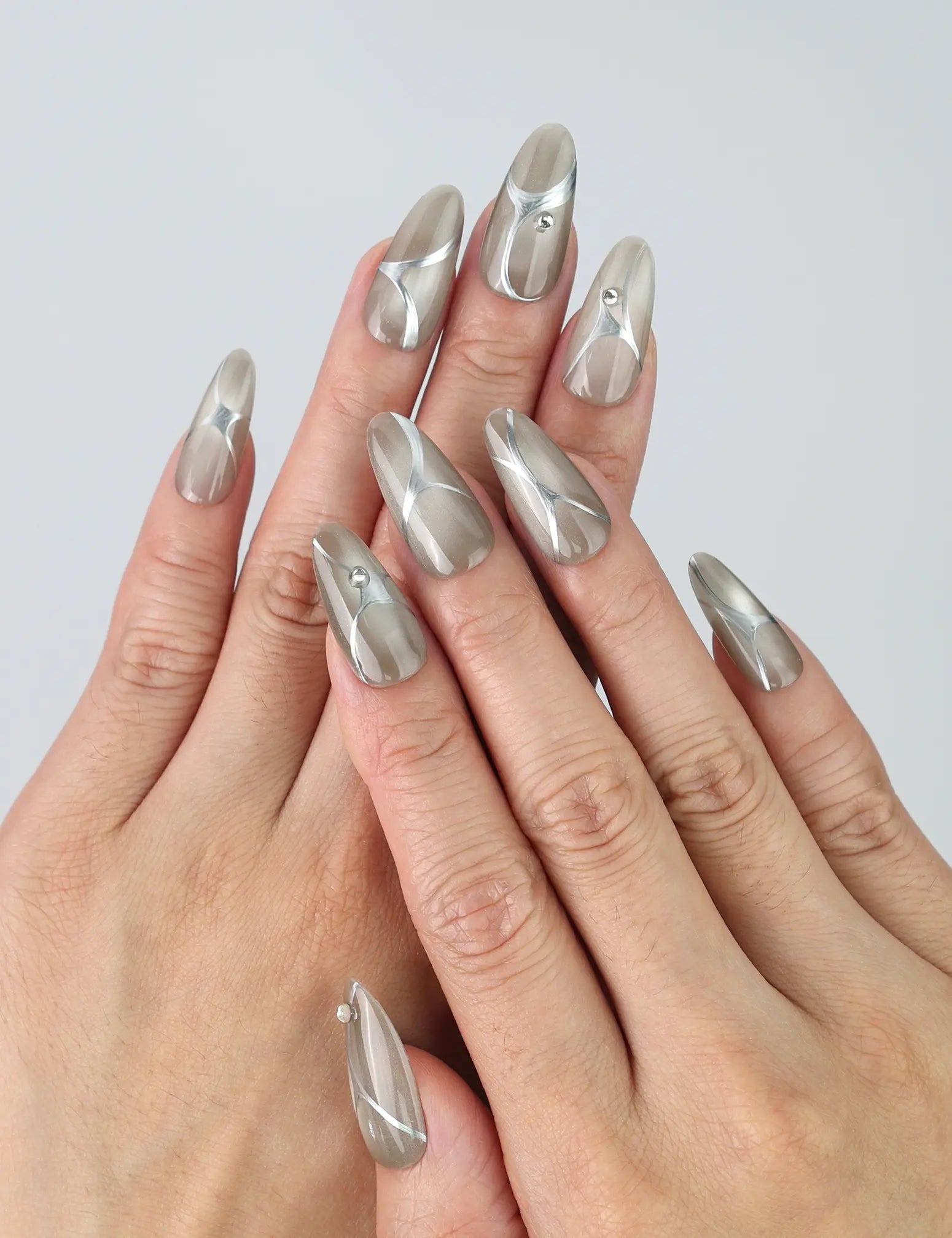 Hand gesture showing medium-length silver press on nails with metallic chrome shine and gem accents by Naillover