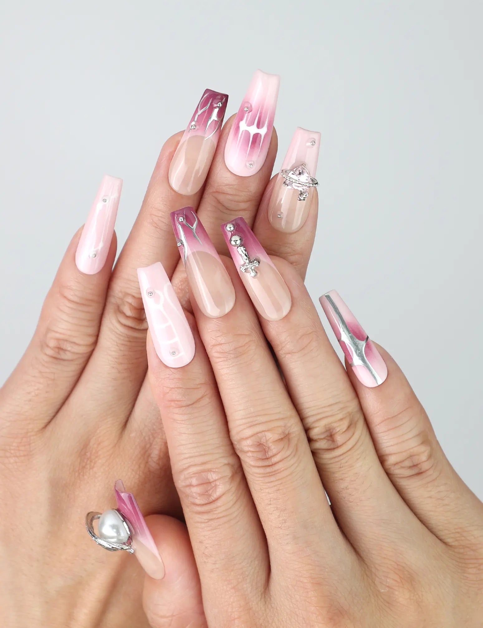 Hand model wearing pink coffin-shaped press-on nails with marble detailing, nude gradient, and silver gemstone accents