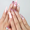 Hand model wearing pink coffin-shaped press-on nails with marble detailing, nude gradient, and silver gemstone accents