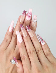 Hand model wearing pink coffin-shaped press-on nails with marble detailing, nude gradient, and silver gemstone accents