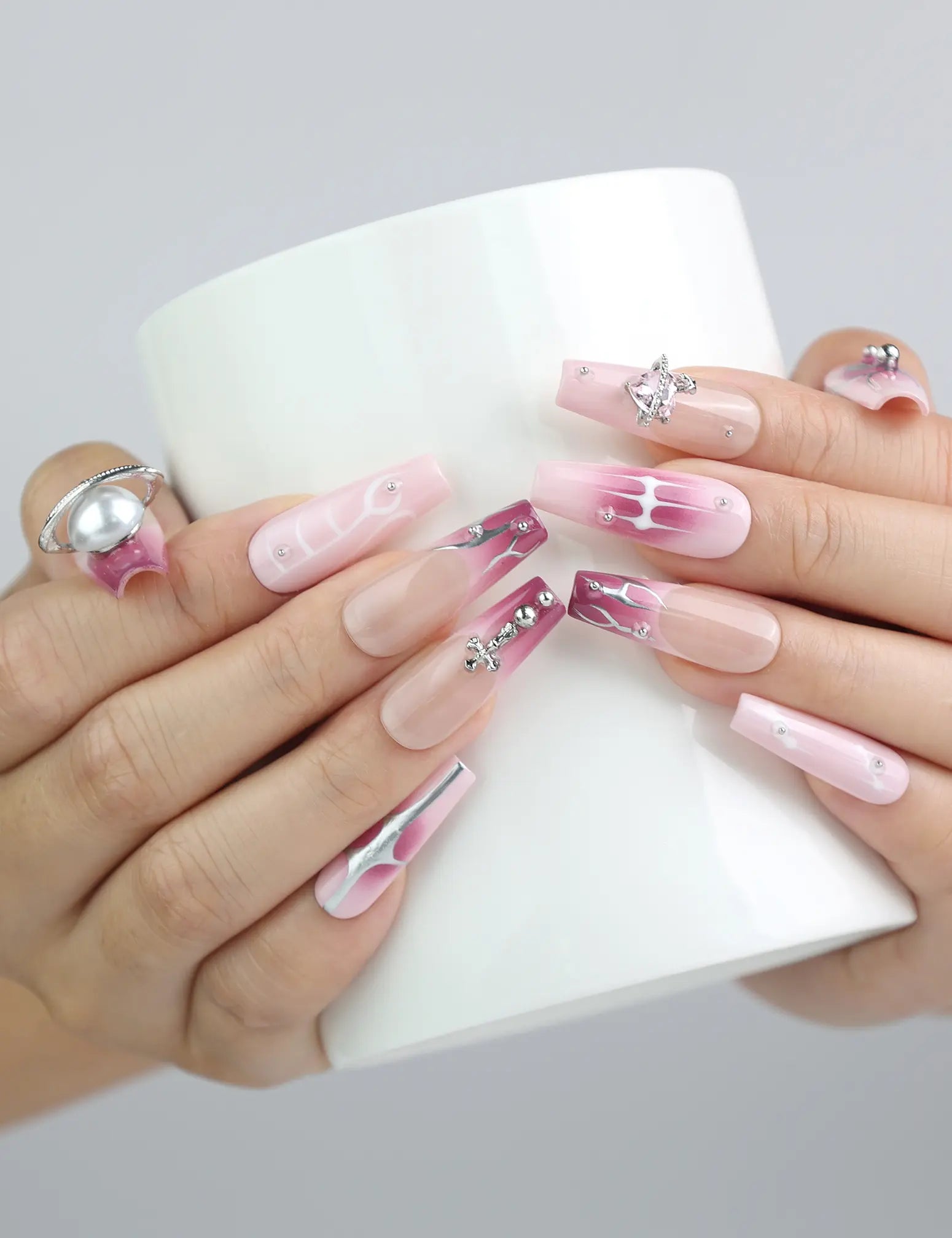Hand holding a cup, showcasing Naillover’s pink coffin nails with glossy marble finish and statement silver gemstones