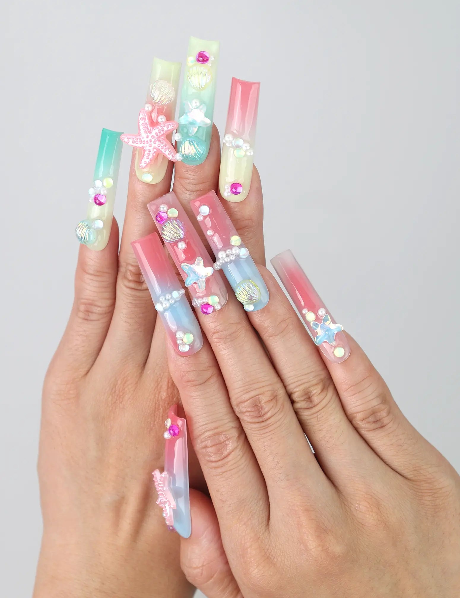 Hand gesture showcasing Singapore handmade long pipe press on nails with 3D floral art, ocean wave designs, and gold starfish accents by Naillover