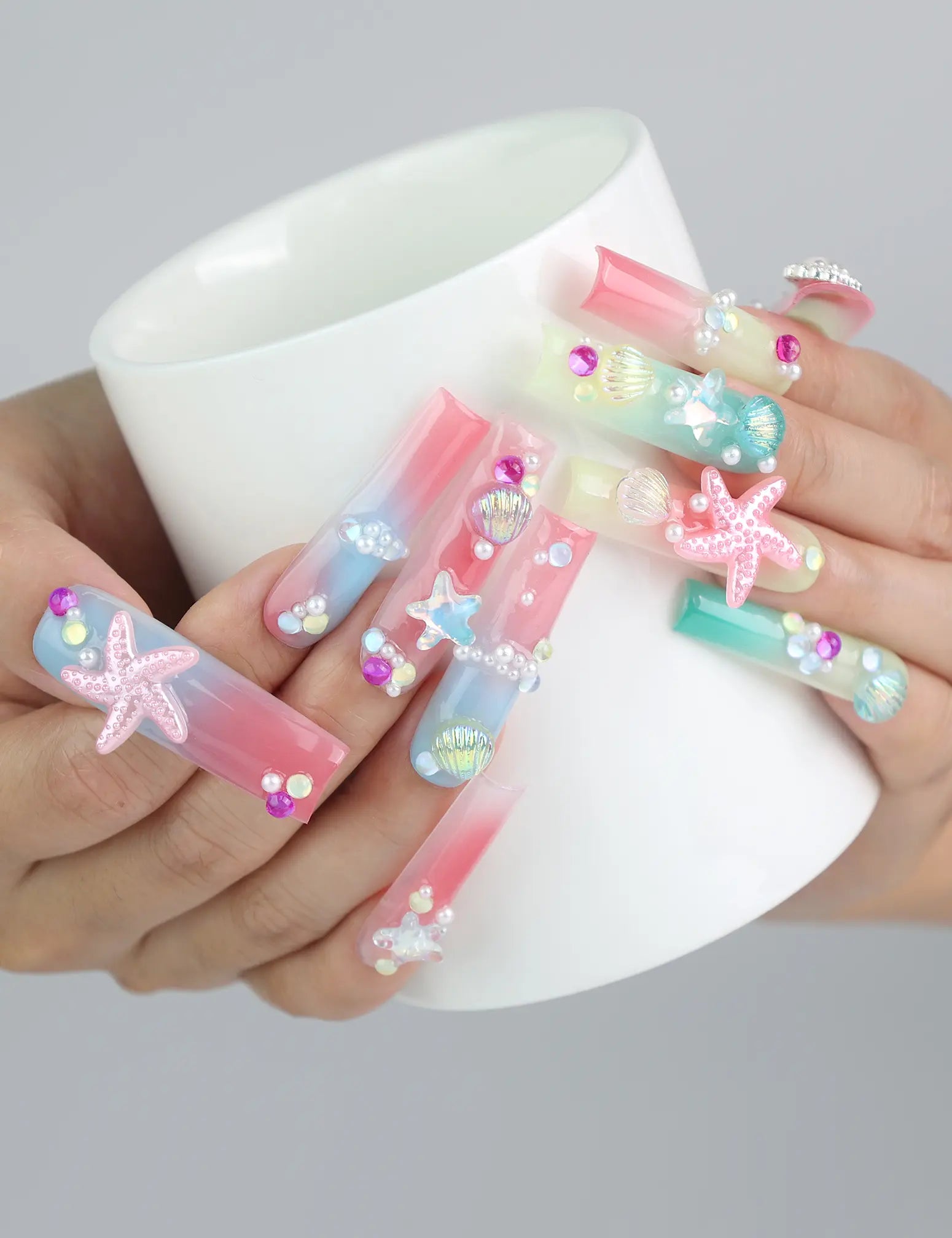 Hand holding a cup while wearing tropical ocean-themed long pipe press on nails with 3D elements and gold accents by Naillover