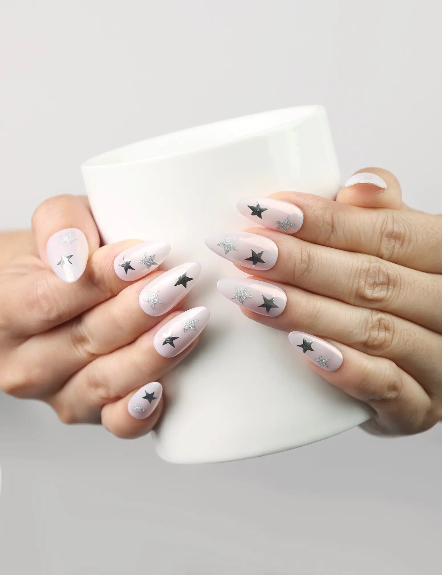 Hand holding a cup wearing Ethereal Stars light pink press-on nails with silver stars, Singapore handmade nails by naillover