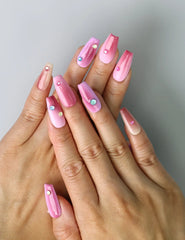 Hand model wearing medium coffin nails with pink-to-red ombré gradient and dazzling gem accents