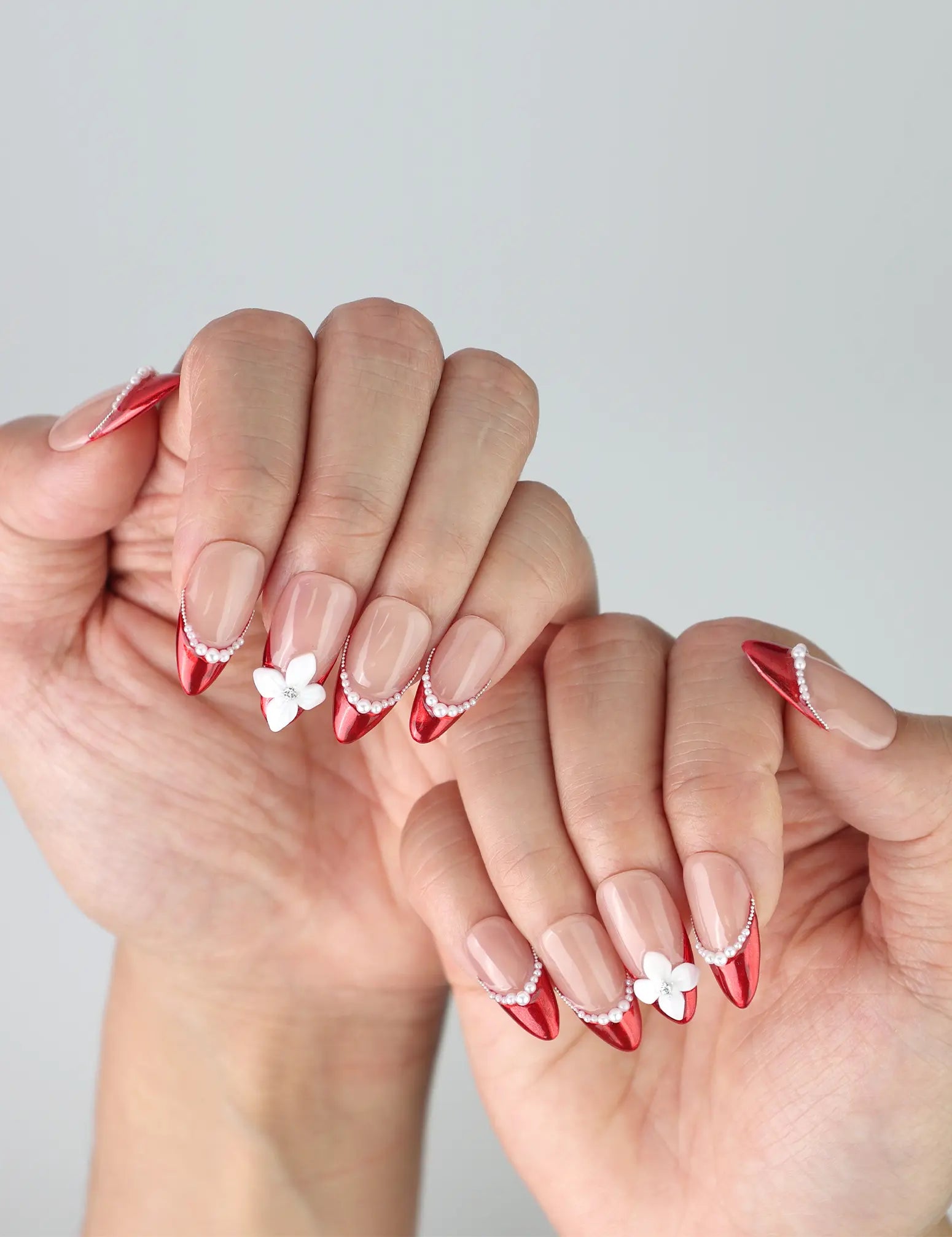 Side view of almond red nails with gradient pink base, showcasing handcrafted flowers and pearl accents