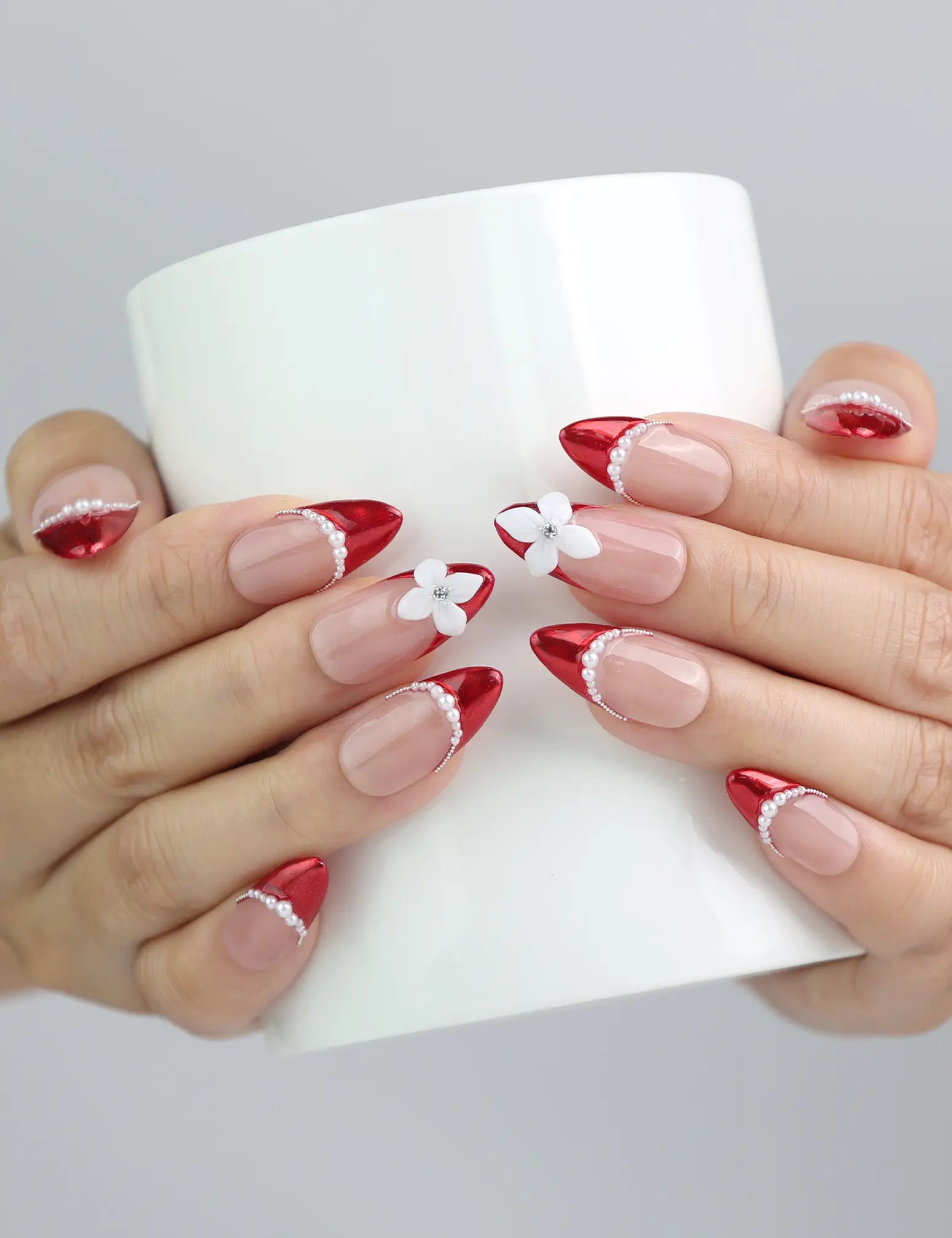 Hand holding a cup, highlighting Naillover’s romantic red and pink almond nails with 3D floral design and pearls