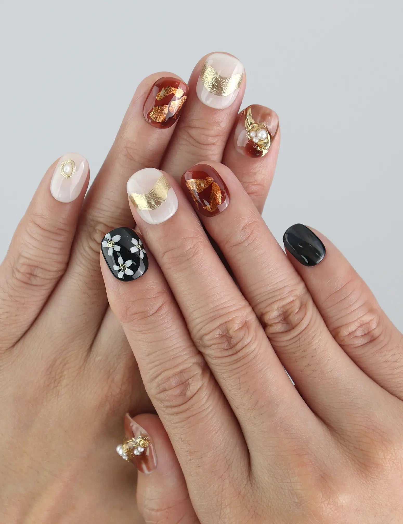 Model wearing Floral Glow Naillover press on nails, showing floral detailing and pearl accents on mixed neutral tones.