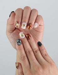 Hand close-up of Naillover Floral Glow nails with golden lines and black floral patterns for a trendy, refined look.
