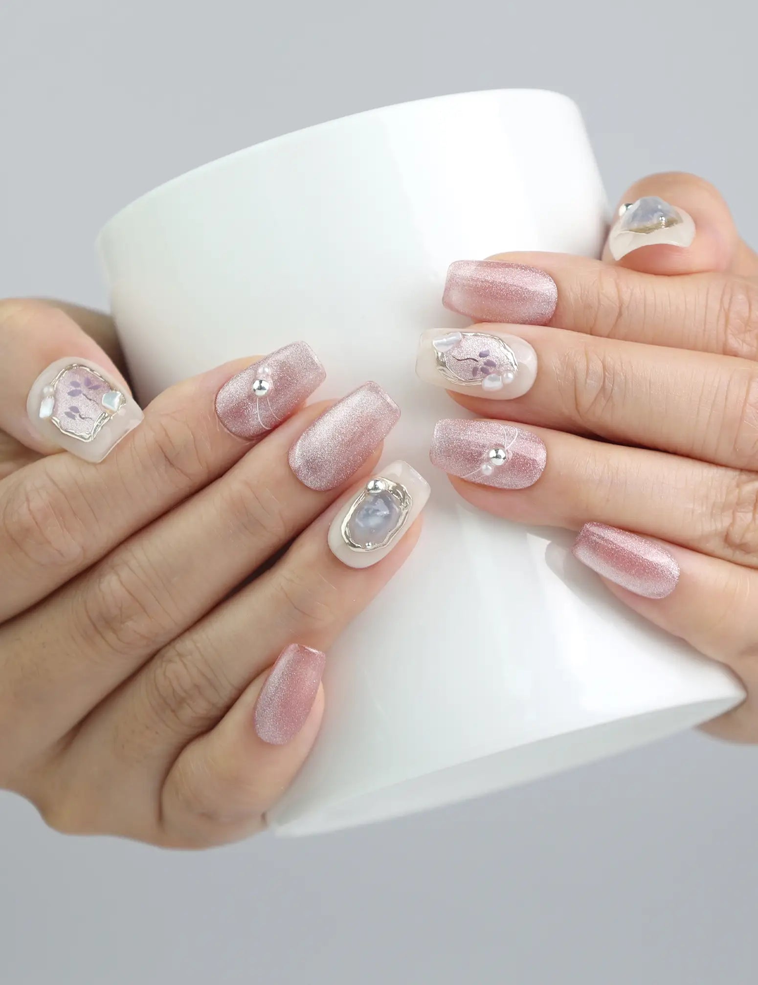 Hand holding a cup while wearing glittery pink and white gradient press on nails with 3D floral accents by Naillover