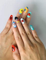 Hand model wearing short handmade nails with retro color palette, smiley emojis, peace signs, and daisy accents