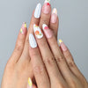 Hand model wearing pink almond-shaped press-on nails with hand-painted floral details and playful fruit elements
