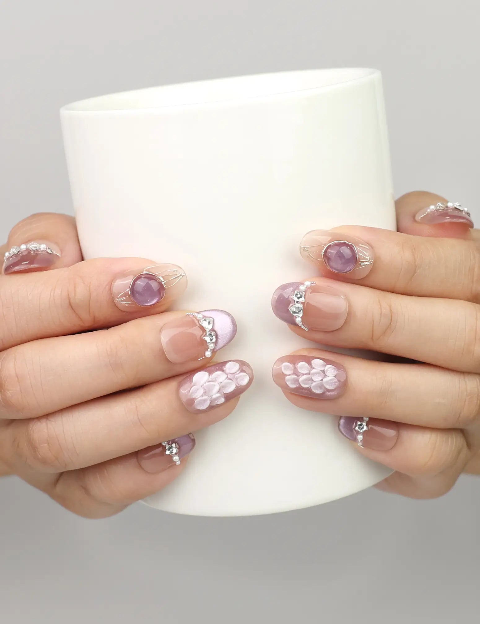 Hand holding a cup while wearing Naillover Gemstone Latte handmade press on nails in shimmering ocean tones with seashell and pearl accents.