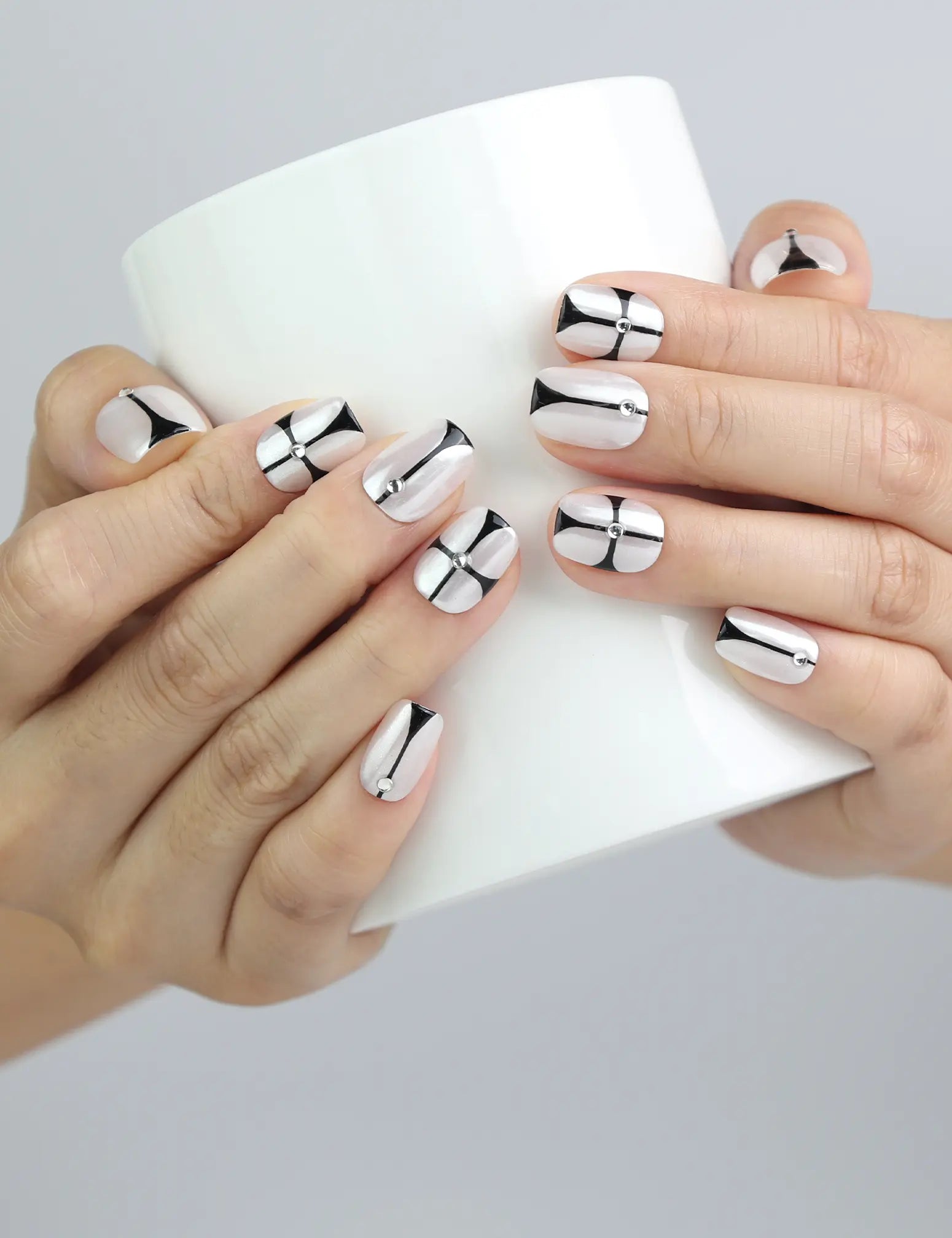 Hand holding a cup, featuring Naillover’s short squoval press-on nails with clean nude polish and chrome black graphic design