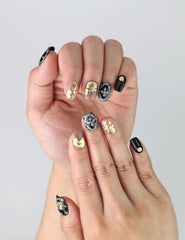 Fingers displayed wearing Singapore handmade black press on nails featuring delicate gold flowers, white petals, and sparkling rhinestones