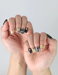 Close-up of hands with black press on nails adorned with golden leaves and 3D floral and rhinestone details, crafted by Naillover