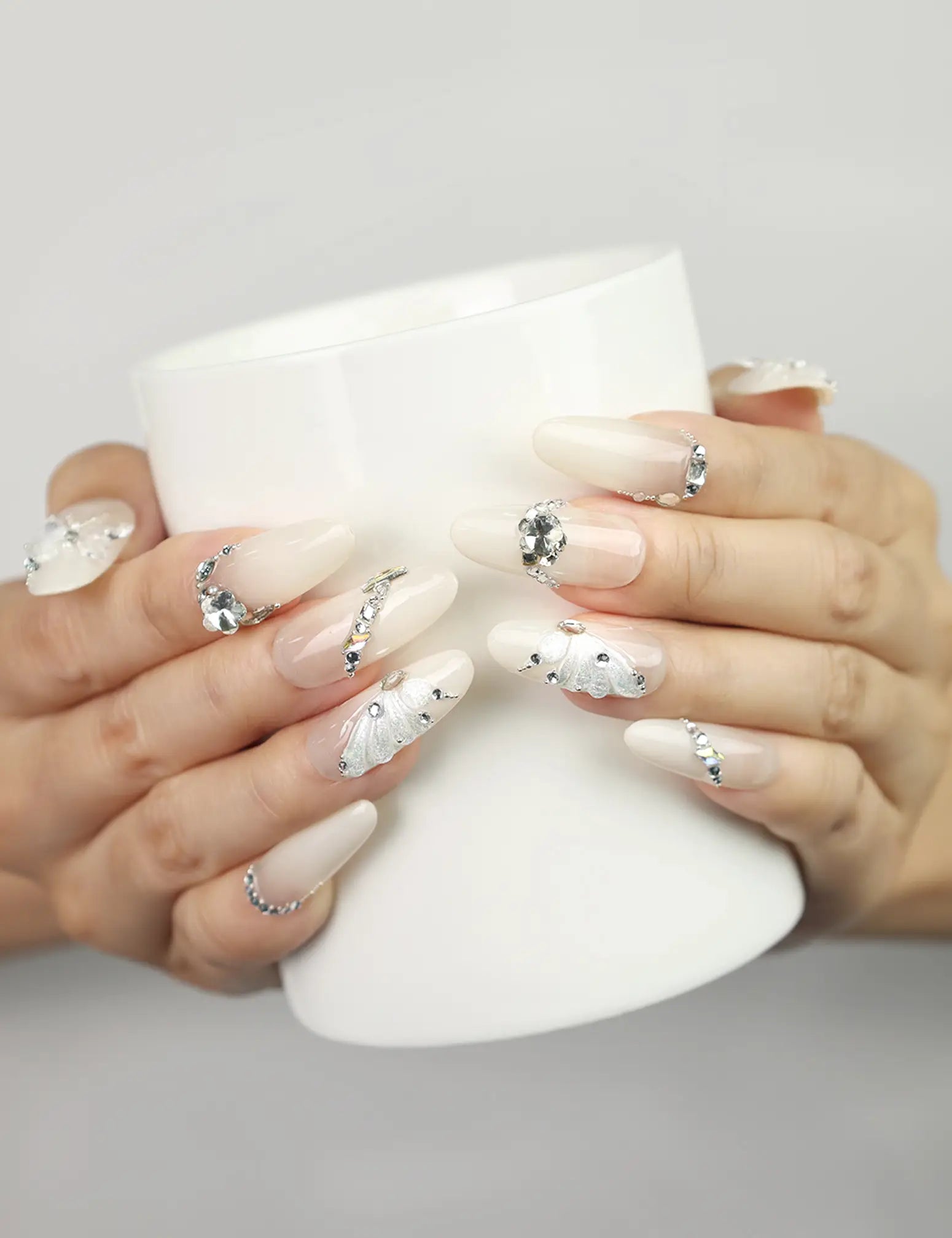 Hand holding a cup wearing Glimmer Mirage translucent handmade Singapore press-on nails with silver glitter and butterfly accents by naillover