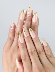 Hand model wearing almond-shaped nude press-on nails with delicate gold line and foil accents
