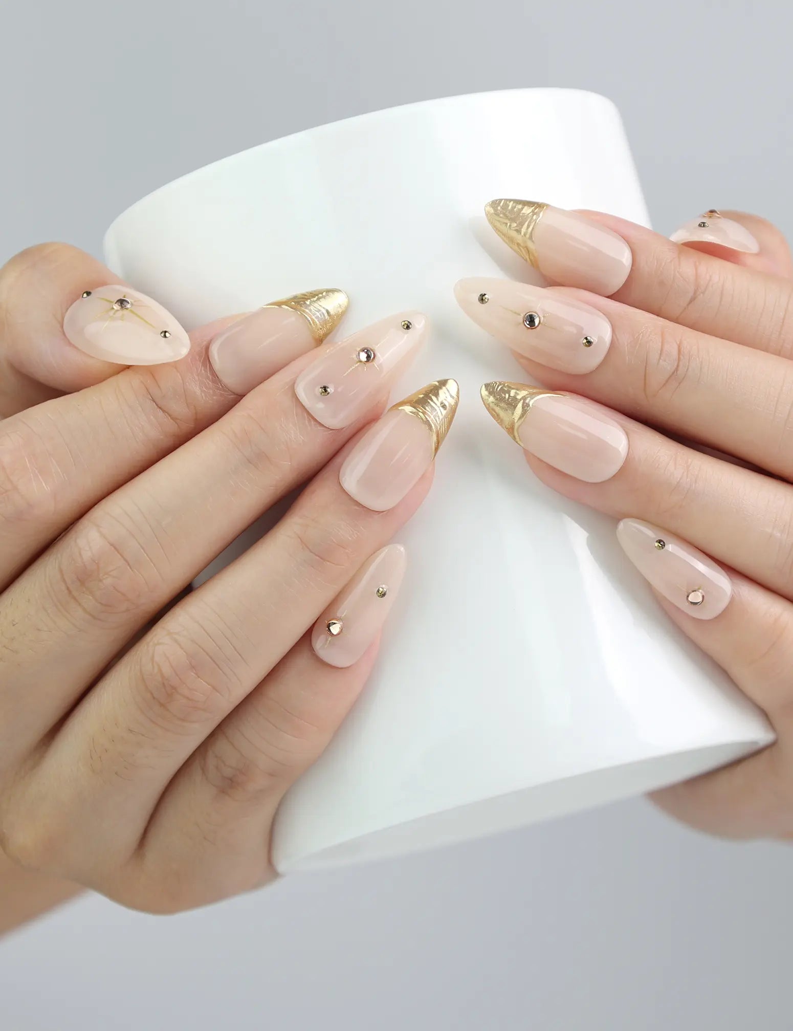 Hand holding a cup, showing Naillover’s nude almond press-on nails with elegant gold accents for everyday wear