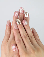 Hand model wearing bold red square press-on nails with shimmering gold foil and sculpted floral accents
