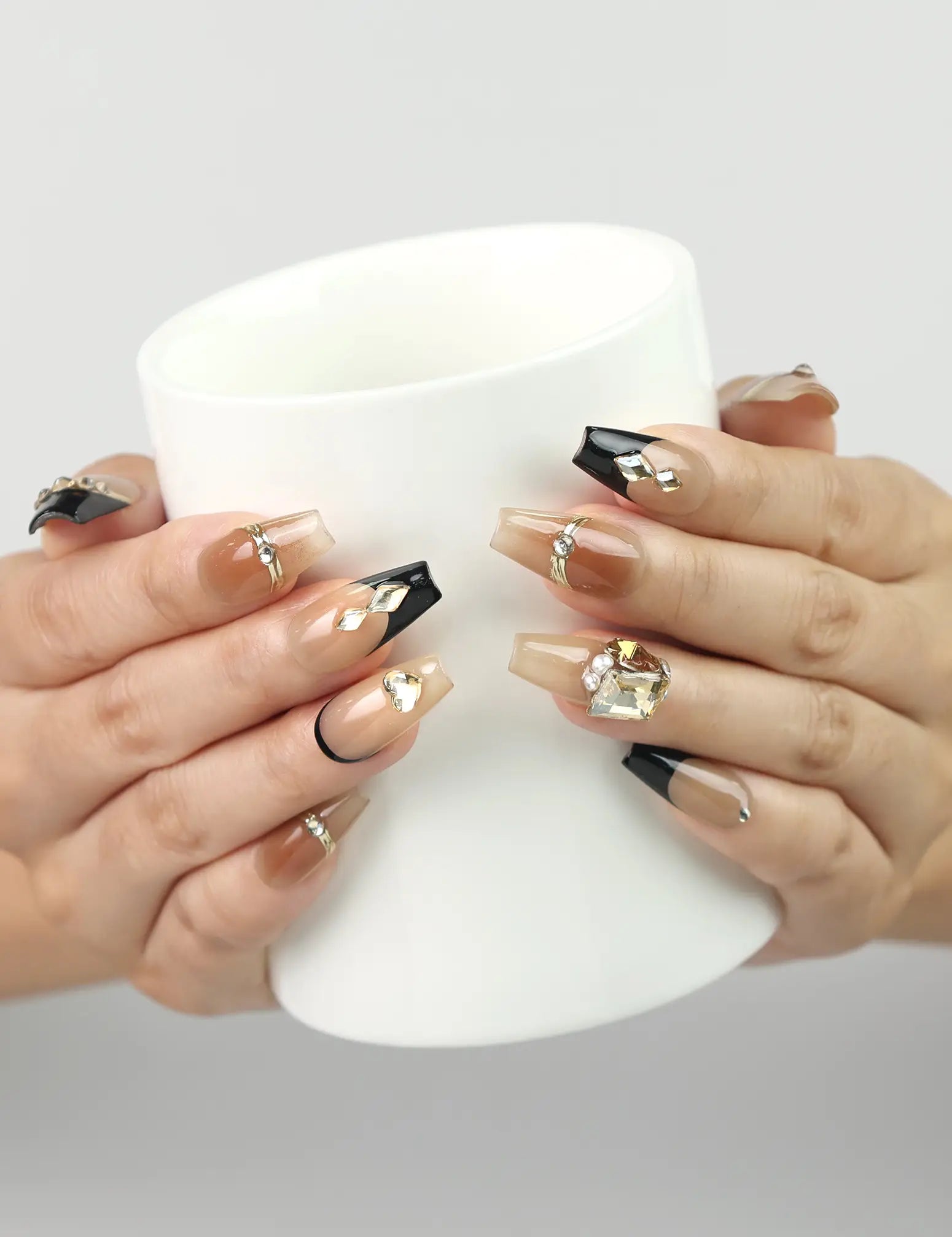 Model holding a coffee cup wearing Gold Tips Singapore press on nails with nude base, gold details, and pearl embellishments – handmade by naillover
