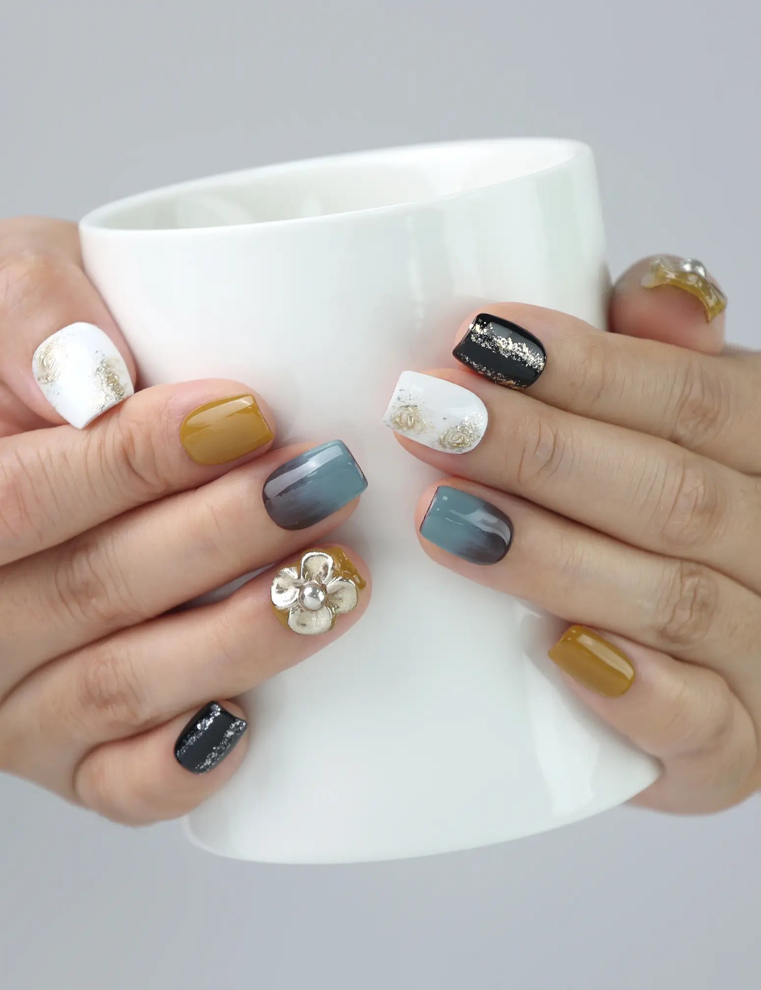 Woman holding coffee mug wearing Golden Bloom Naillover press on nails, featuring cozy fall vibes and golden flower charm.