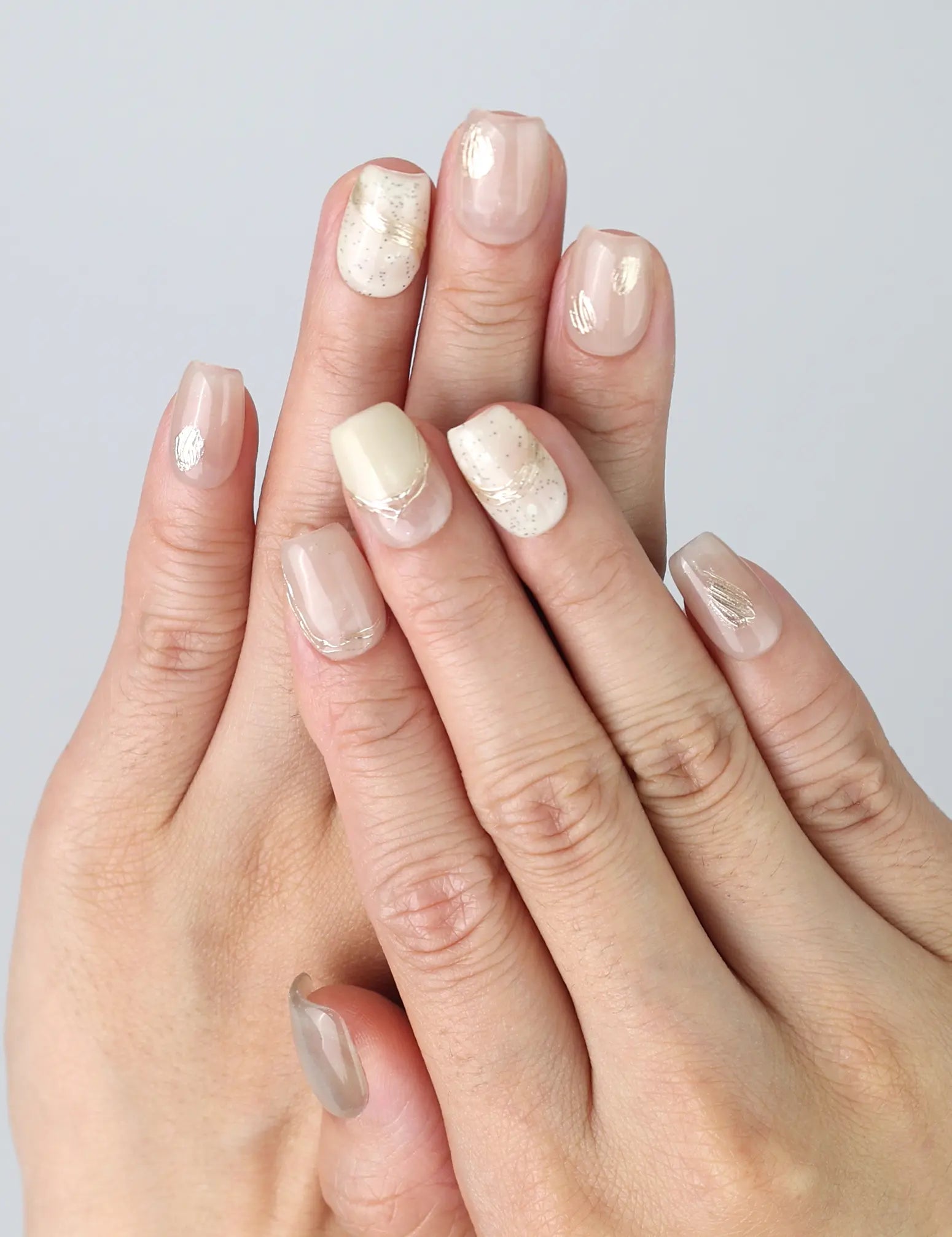 Hand gesture showcasing pale pink short press on nails with fine gold lines and soft shimmer, handmade in Singapore by Naillover