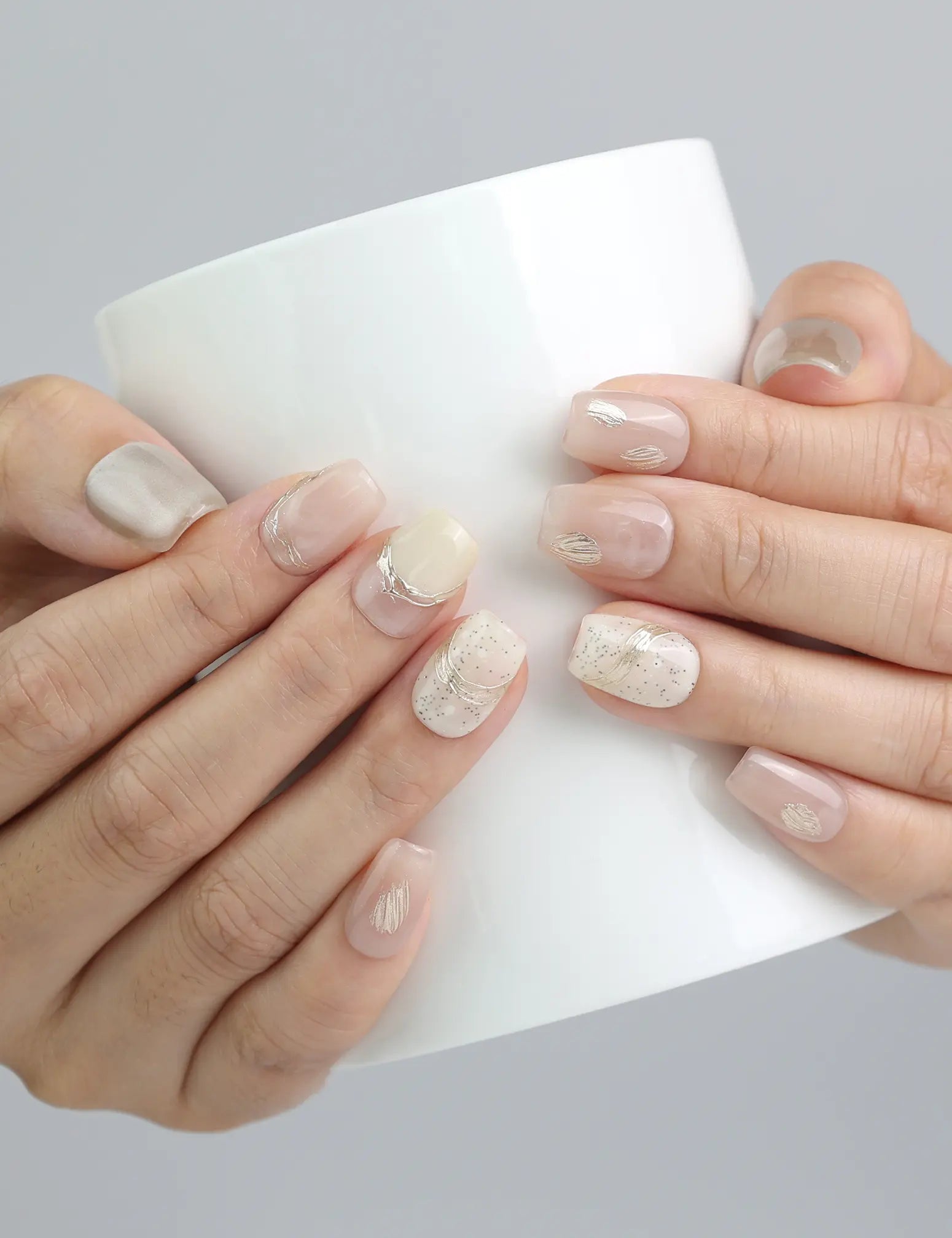 Hand holding a cup while wearing pale pink press on nails with fine gold accents and shimmer, handcrafted by Naillover