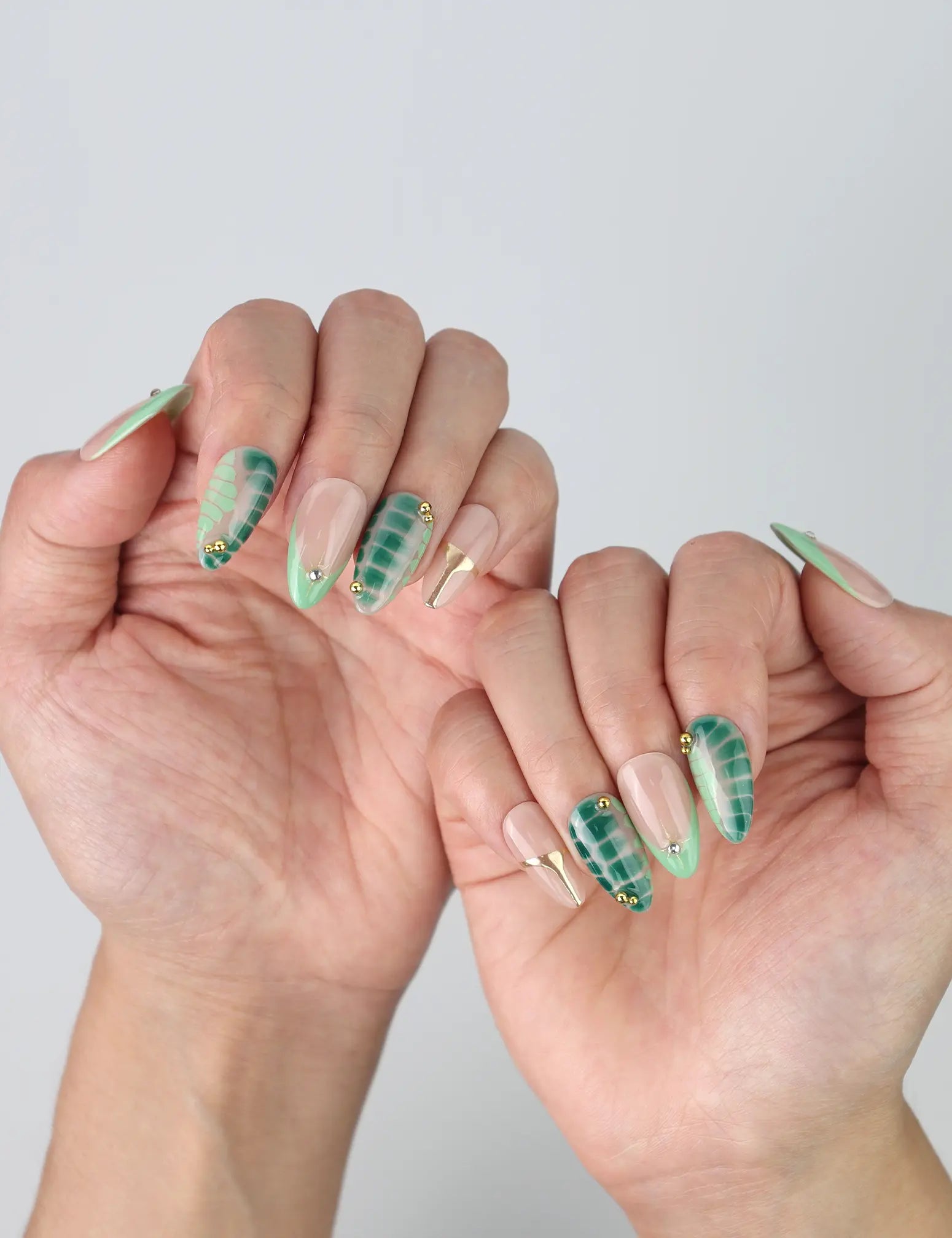 Side view of Naillover short almond press-on nails with fresh green foliage art and elegant metallic gold detailing