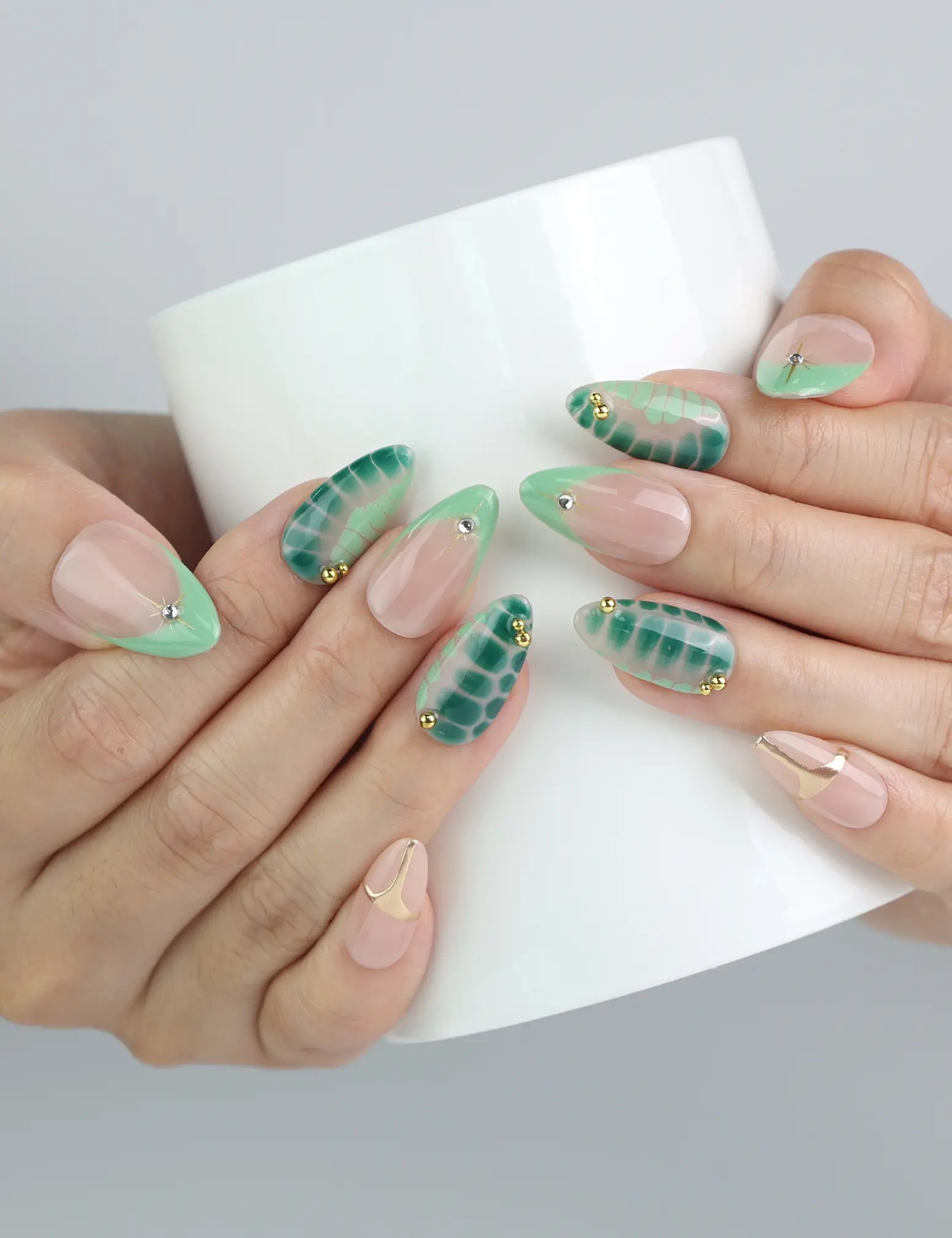 Hand holding a cup, showcasing handmade nude and green nails with botanical leaf art and subtle gold embellishments