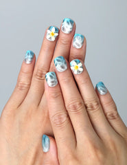 Hand model wearing short squoval press-on nails with soft blue ombré gradient and dainty white flower accents