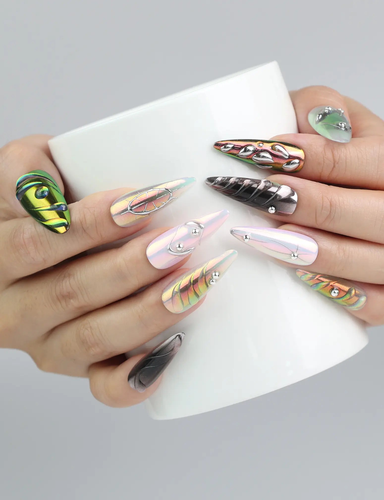 Hand holding a cup while wearing vivid multicolor chrome stiletto nails with embedded gems for a glam touch