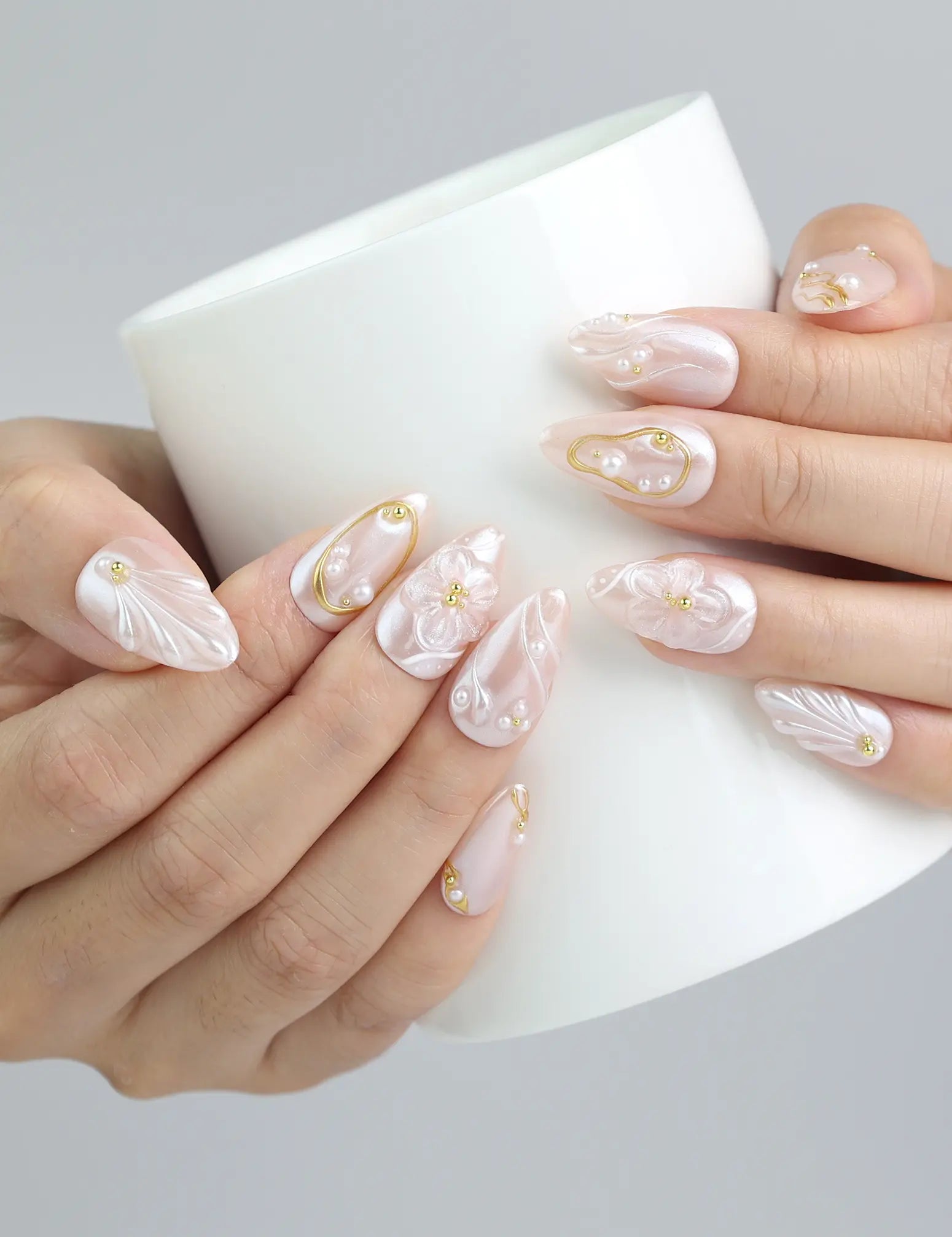 Holding a cup with Singapore handmade pastel pink press on nails with raised floral designs and gold touches by Naillover