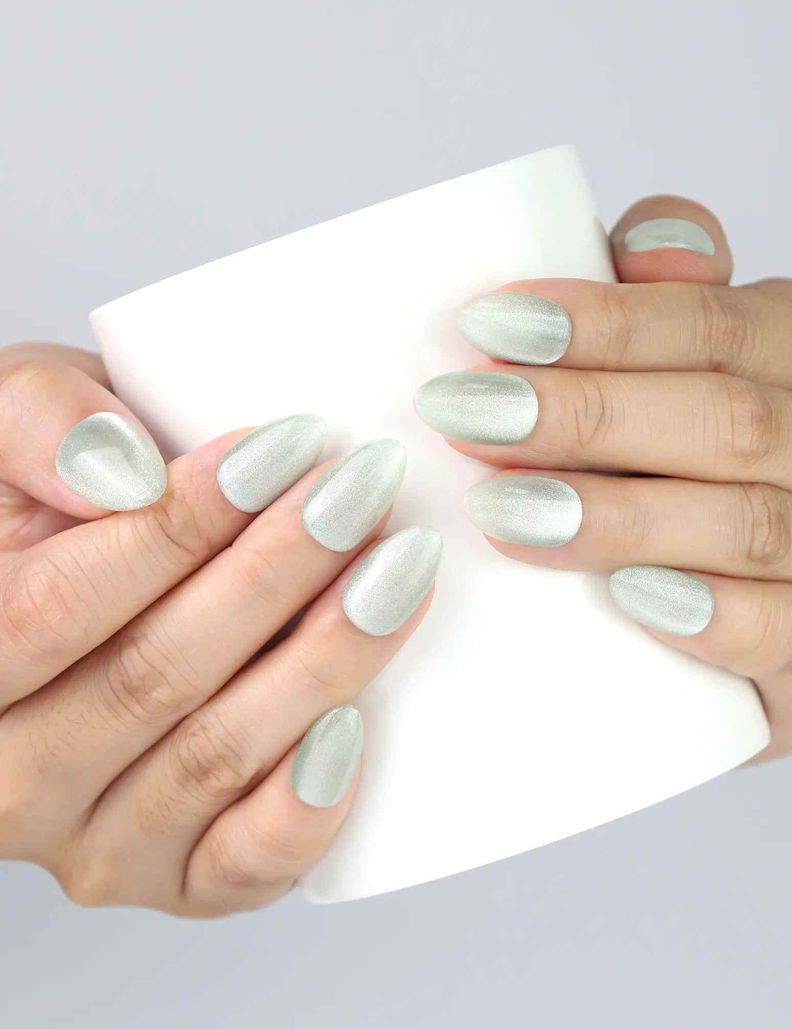 Hand holding a ceramic cup, showcasing Naillover Jade Curve press on nails in jade green cat eye finish.