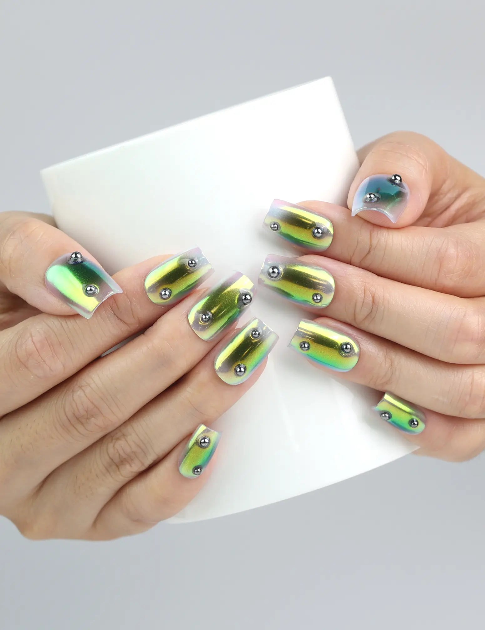 Hand holding a cup, showcasing Naillover’s short square press-on nails in glossy green chrome with jewel-toned shine