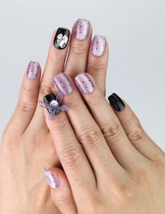 Hand model wearing short square press-on nails in black and purple with kawaii heart-shaped gems and playful accents