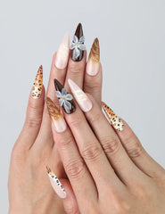Hand model showing stiletto nails with bold brown leopard print, matte black accents, and delicate floral designs